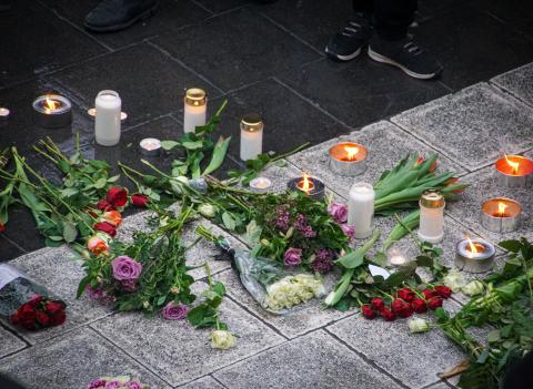 Bouquets of flowers and candles are arranged on the ground as a memorial.