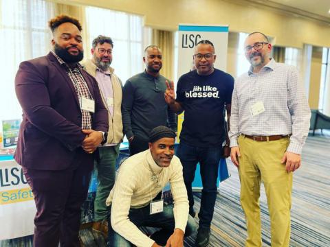 A group of men pose in front of a booth at a conference.